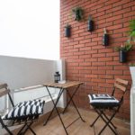 Terrace with table and chairs and flowers on the red brick wall.