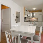 Dining area and fully equipped kitchen behind it. On the right is the entrance to the living room.